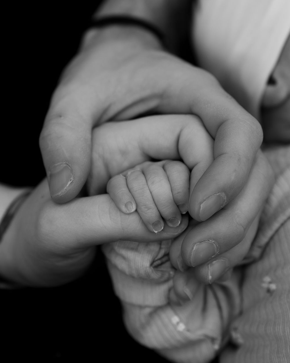 Black and white close-up of adult hands gently cradling a newborn baby's tiny hand.