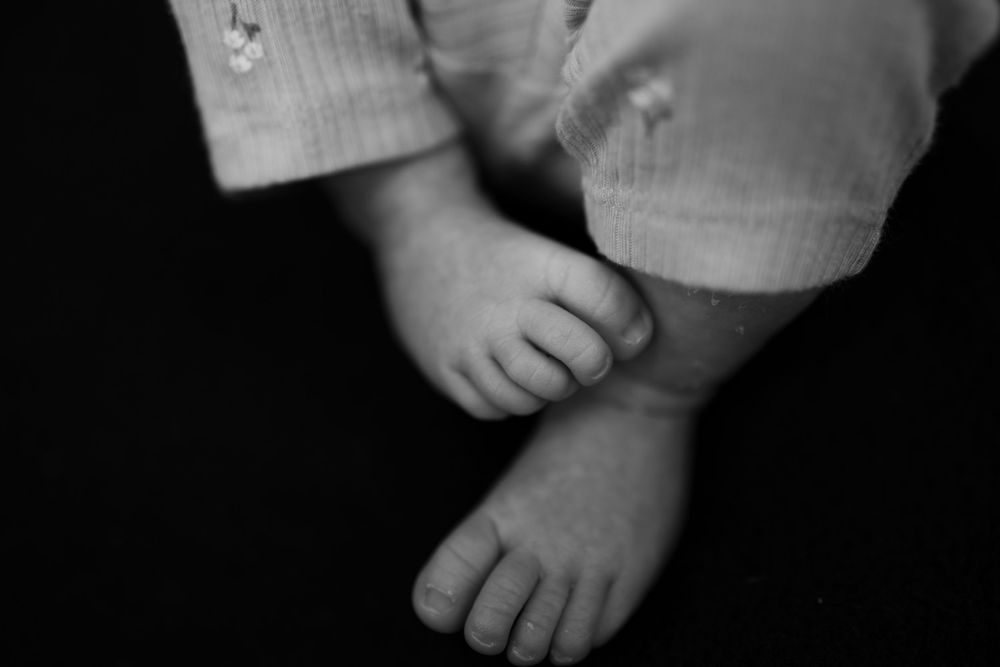 Close-up black and white photo of tiny newborn baby feet and toes on dark background.