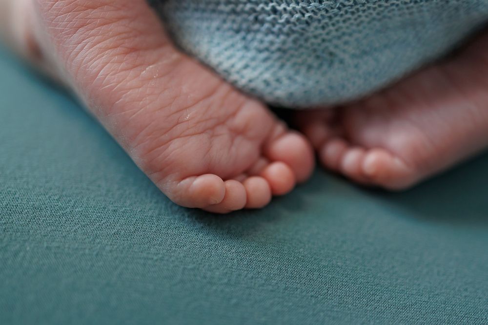 Close-up macro photo of tiny baby feet on a teal textured background.