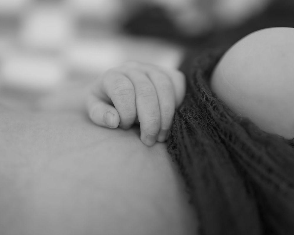 Close-up black and white photo of a tiny baby hand grasping fabric.