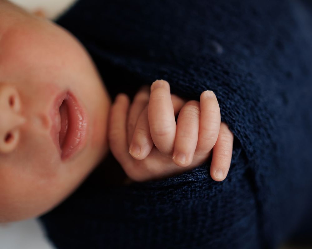 A tiny hand grips the edge of a navy blue sweater in an intimate close-up photograph.