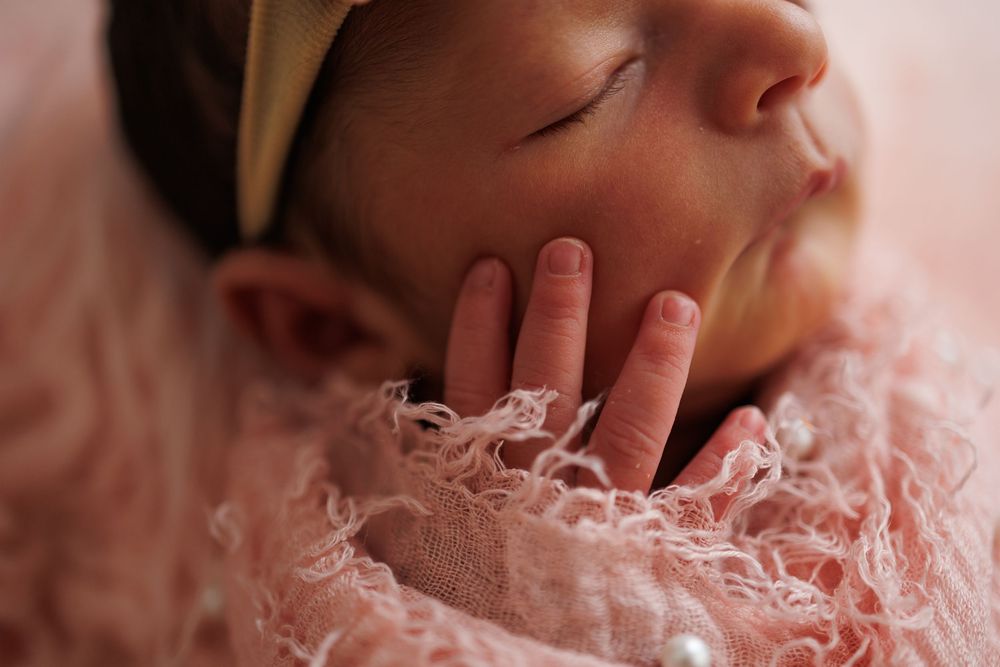 Newborn baby wrapped in soft pink blanket rests peacefully against neutral background in close-up shot.