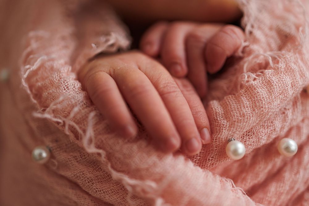 Soft peachy pink crochet fabric texture with pearl bead embellishments shown in close detail.