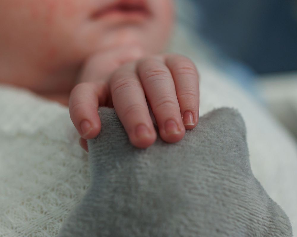 Close-up view of a tiny baby hand resting on soft grey fabric, showing delicate newborn details.