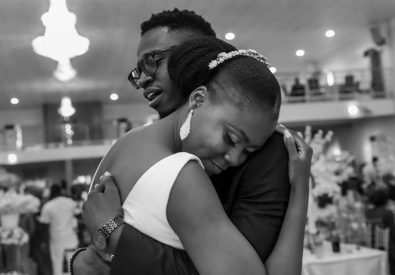 An emotional embrace between two people at an indoor celebration with hanging lights.