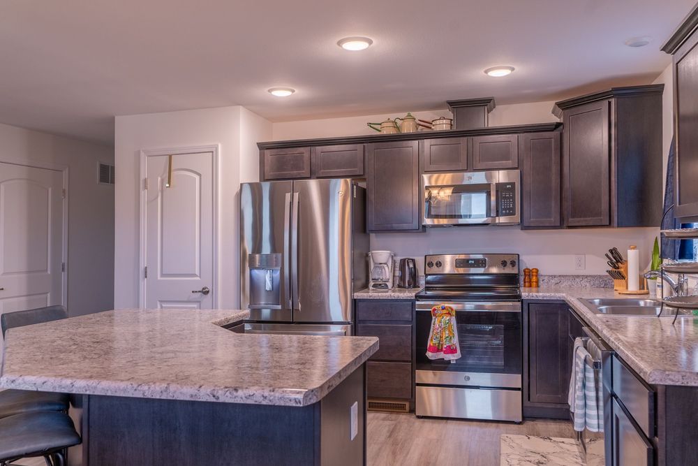 Modern kitchen with dark cabinets, stainless steel appliances, granite countertops and large center island with pendant lighting.