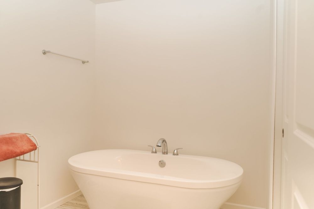 Freestanding white soaking tub with chrome faucet against beige wall in bathroom.