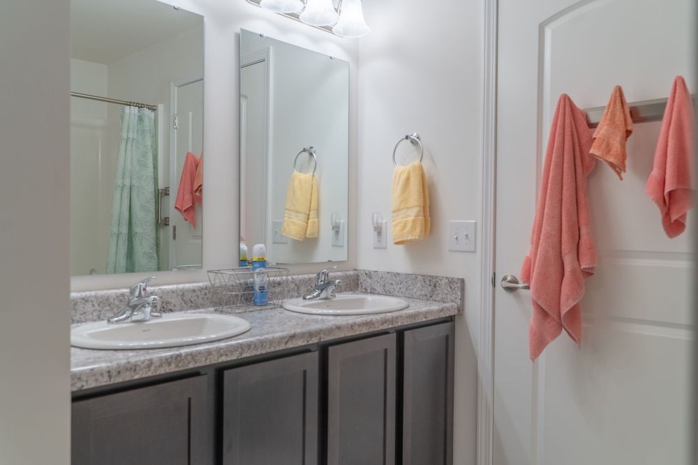 Double vanity bathroom with gray countertops, dark cabinets, large mirror and coral colored towels.