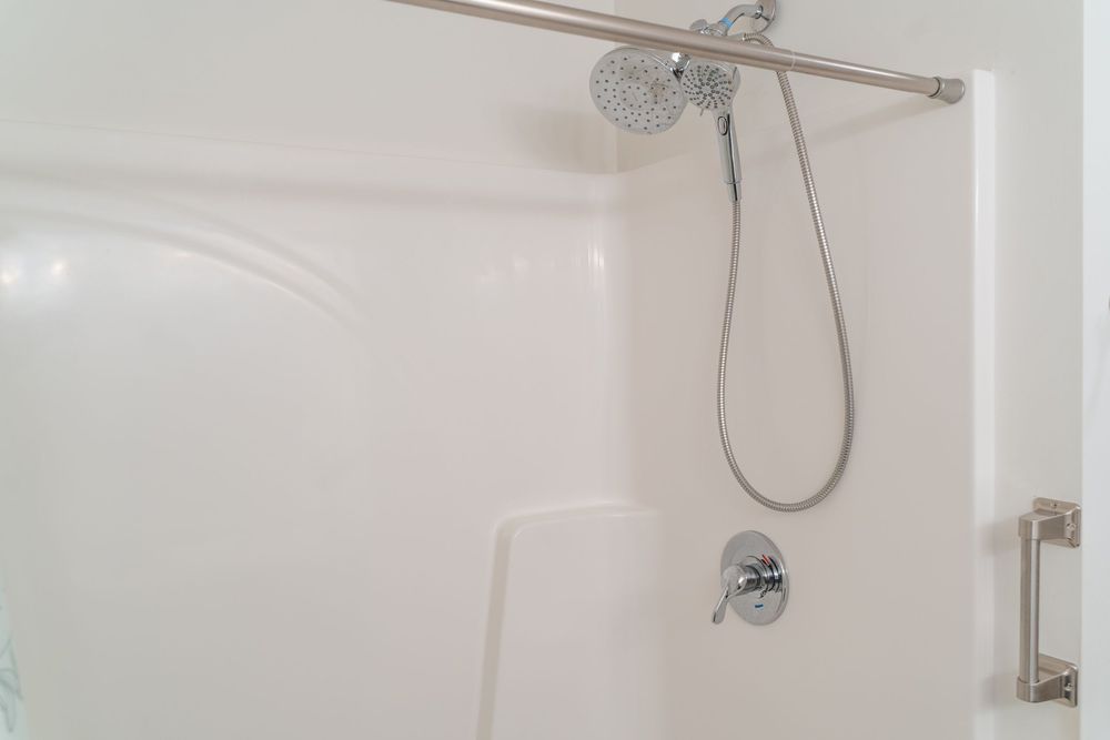Modern shower stall with chrome rainfall showerhead and handheld sprayer.