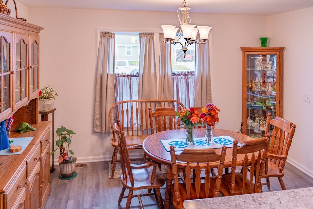Traditional dining room with oak furniture set, light beige walls, chandelier, and curio cabinet displaying collectibles.