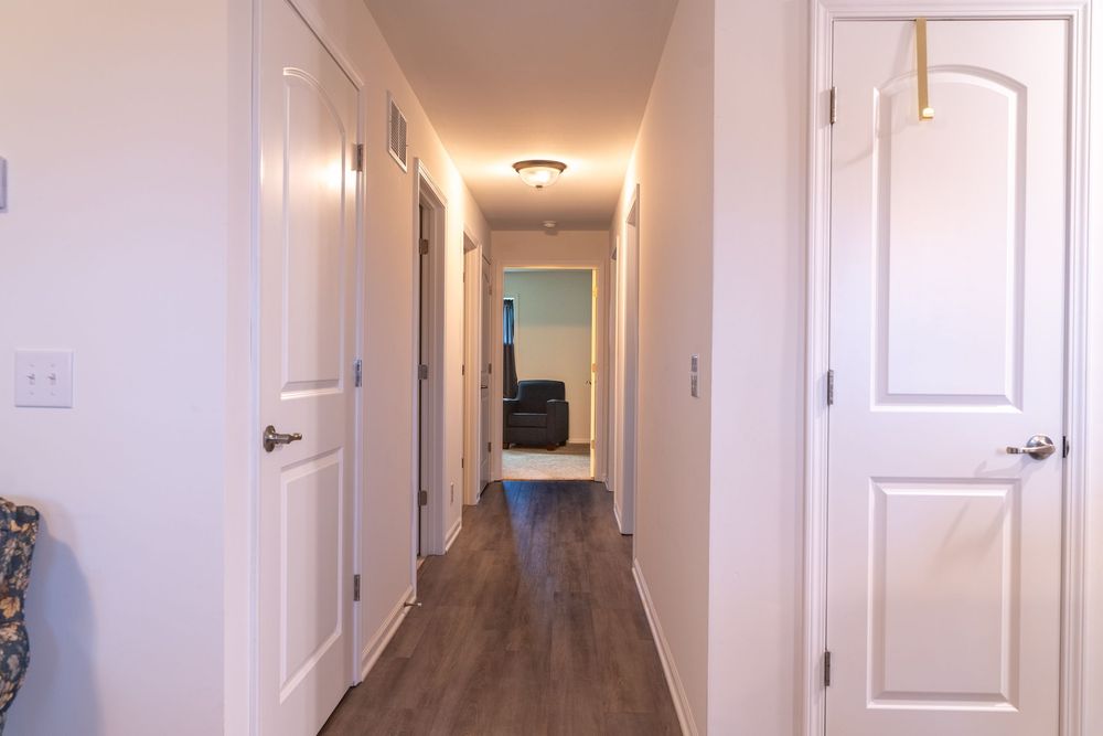 Long hallway with white doors and wood-look flooring leading to a room at the end.