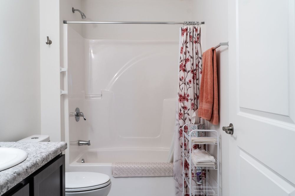 Modern white bathroom interior with floral shower curtain, built-in shelving, and orange towel accent.
