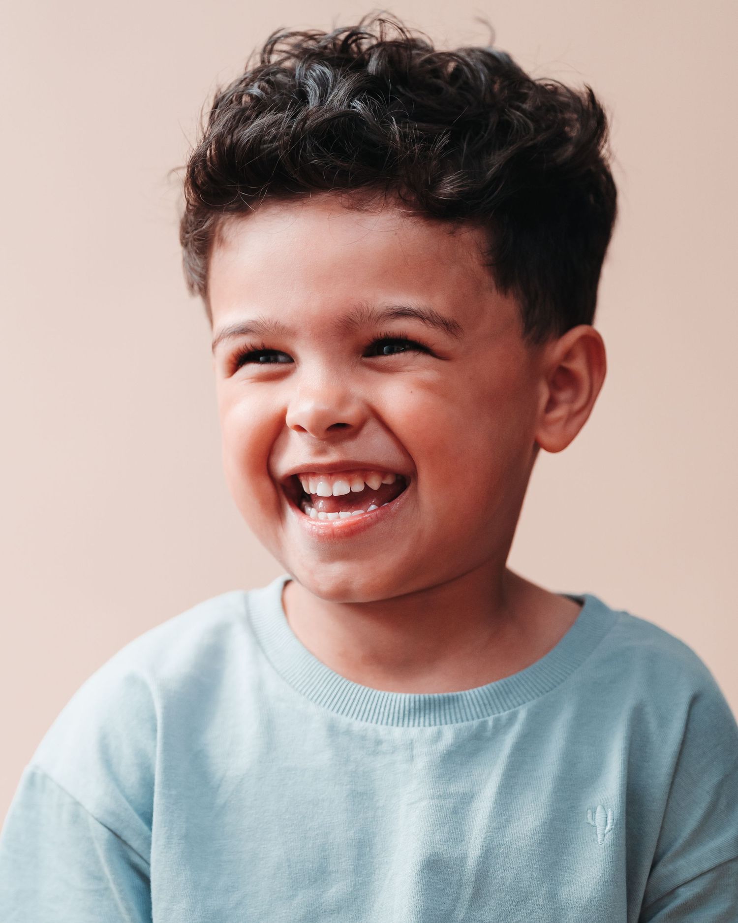 Child wearing light blue shirt laughing joyfully against pink background.