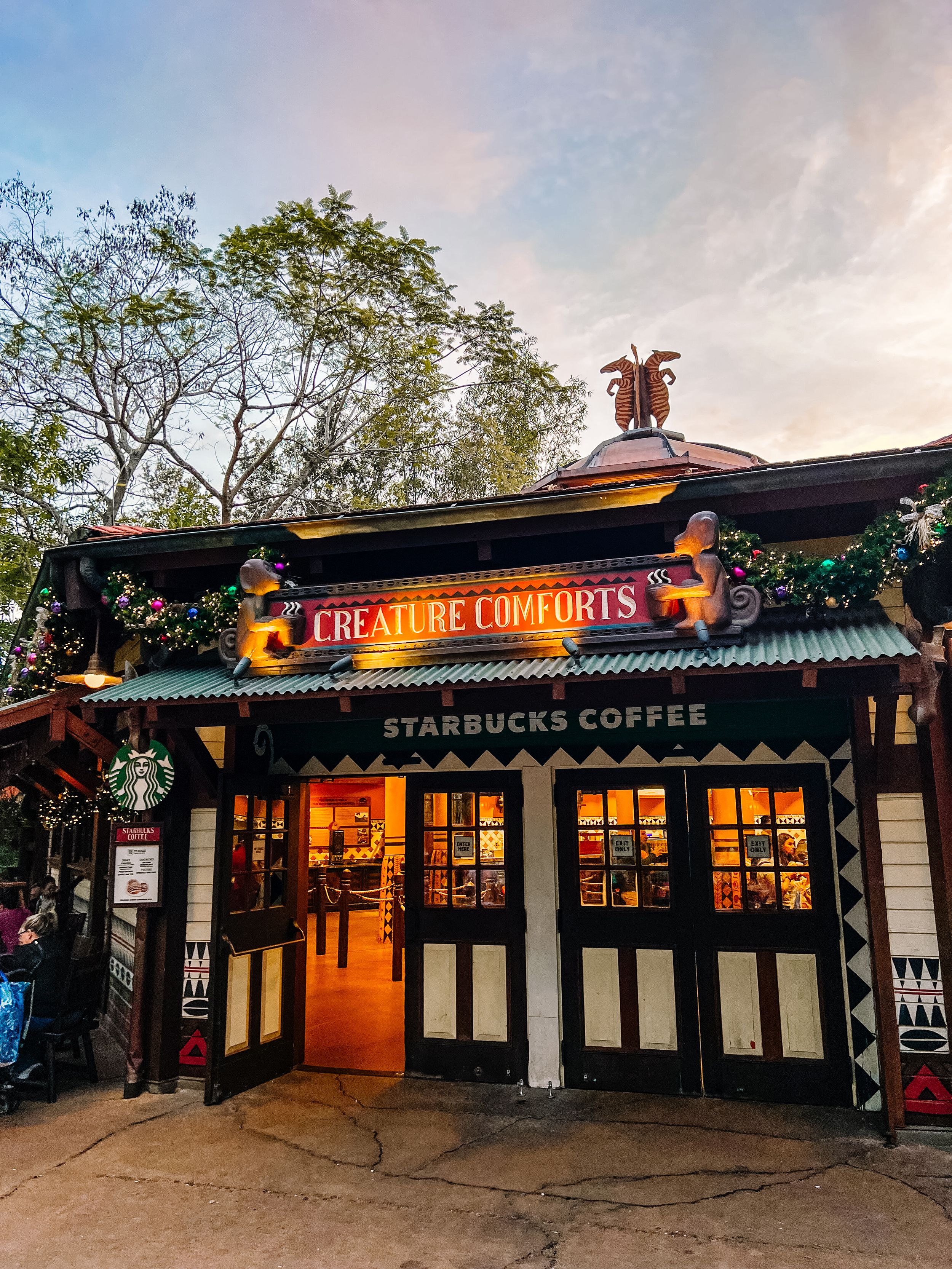 A Starbucks Coffee shop with 'Creature Comforts' signage illuminated at dusk.