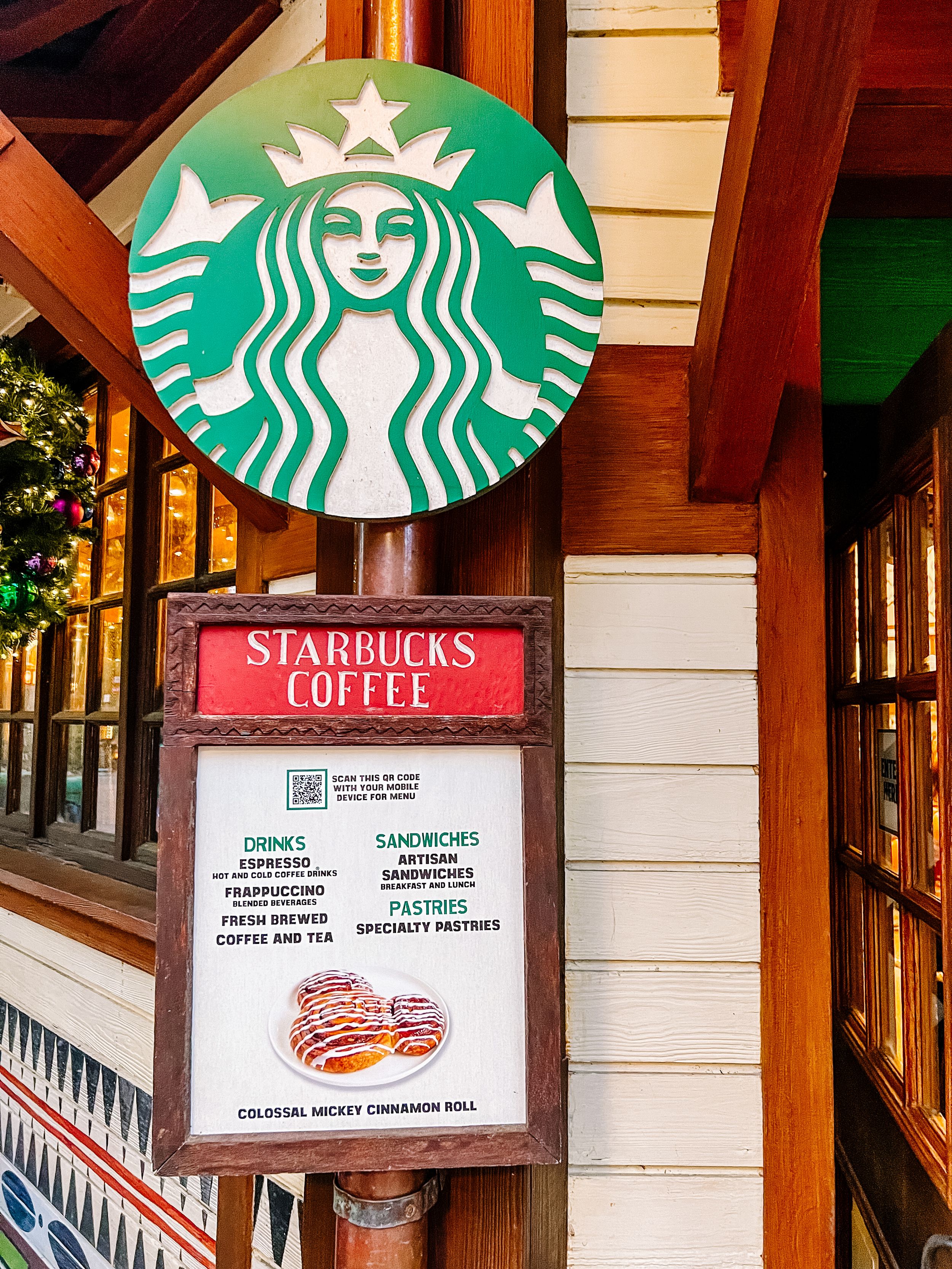 A classic Starbucks logo and menu sign mounted on a wooden building exterior.