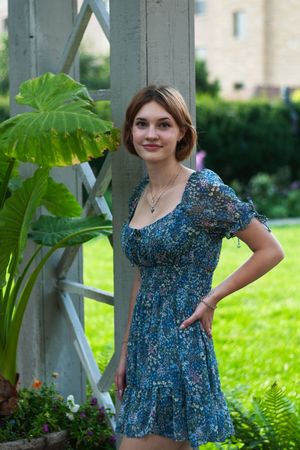 A senior girl leaning against a trellis with plants and grass in the background