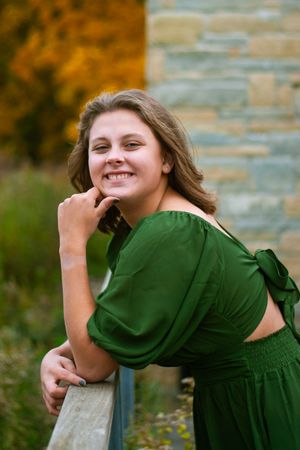 A senior girl in a green dress, smiling and leaning against a railing