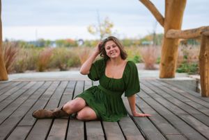 A senior girl in a green dress sitting on a bridge