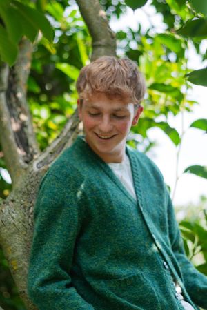 A portrait of a senior boy in a green sweater leaning against a tree