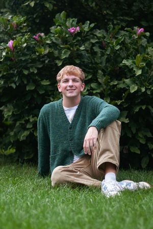 A portrait of a senior boy in a green sweater sitting in a garden
