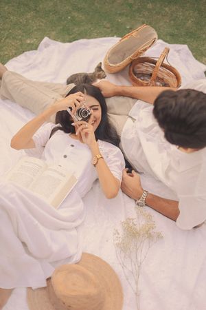 Artistic flat lay of person in white dress lying on blanket with shoes and baby's breath flowers.