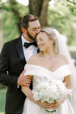 Romantic wedding couple embracing in a garden setting with white floral bouquet.