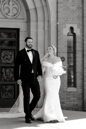 Elegant black and white wedding portraits against a classic brick building with arched architecture.