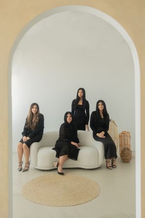 Minimalist group photo with people seated on white couch against beige wall with arched doorway.