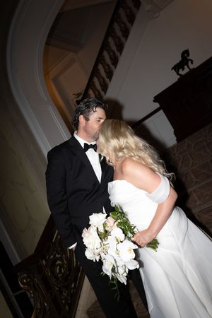 Dramatic wedding couple portrait with white bouquet in low-light setting.