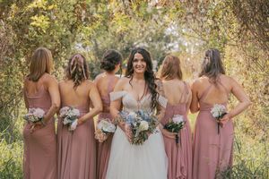 Bridal party in blush dresses poses together outdoors with bouquets.