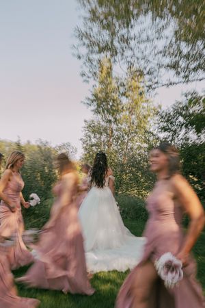Motion blur photo of wedding party in pink dresses dancing outdoors.