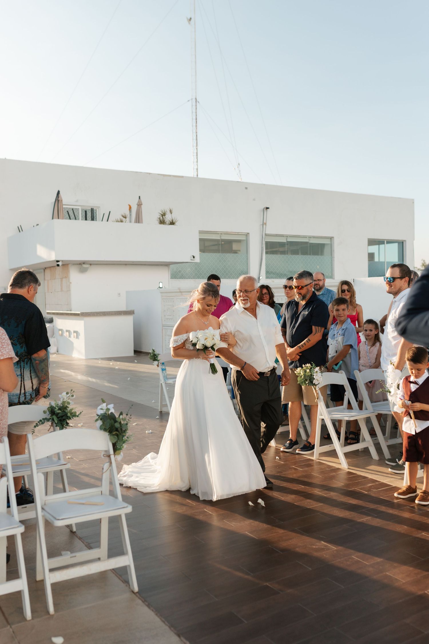Bride walking down aisle with escort at outdoor rooftop wedding ceremony.