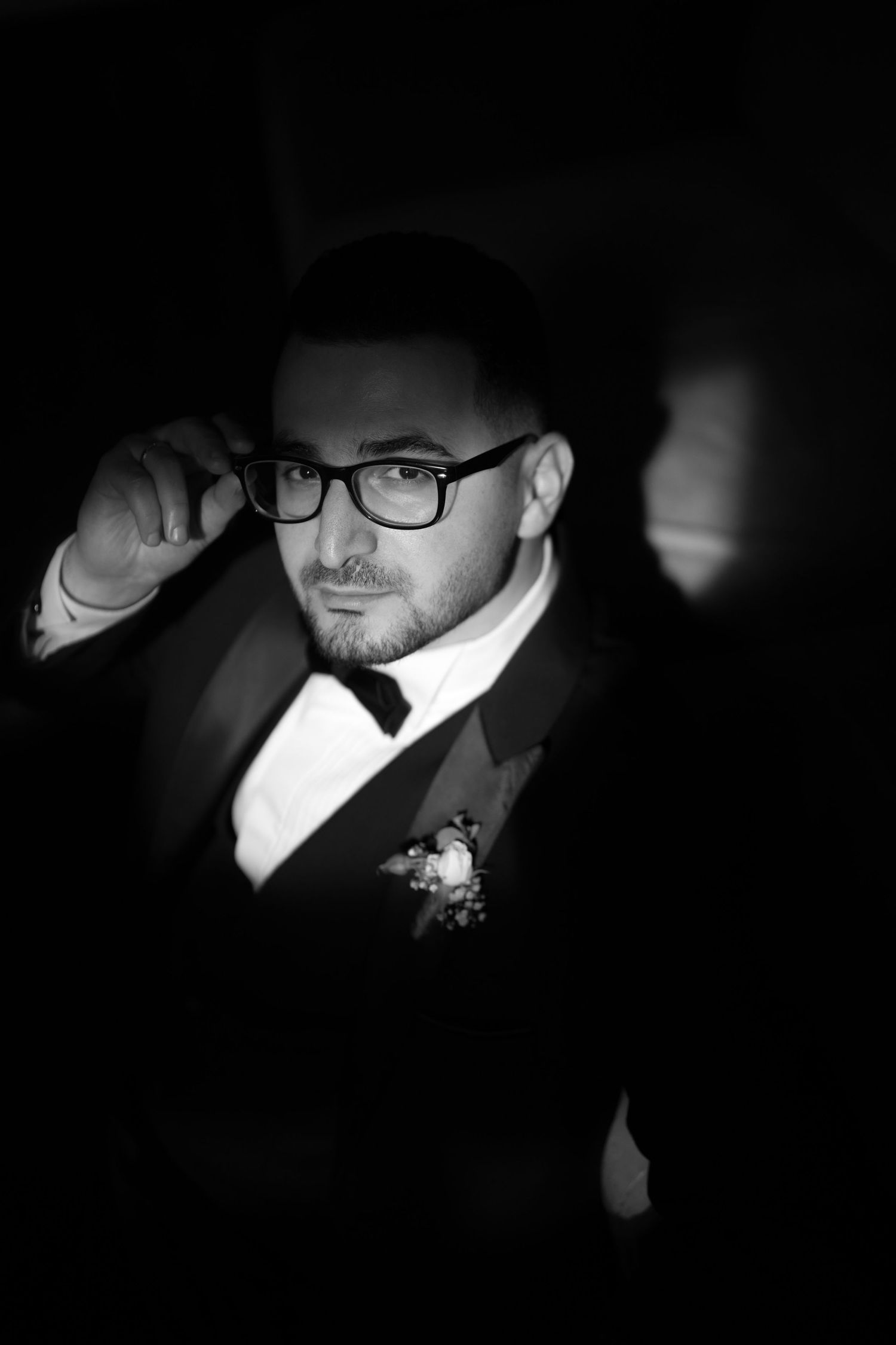 Elegant black and white portrait featuring a person in glasses wearing a dark suit with a boutonniere.