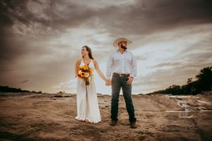 Elopement couple holding hands on rock formation with clouds and sun set in Hill Country, Texas.