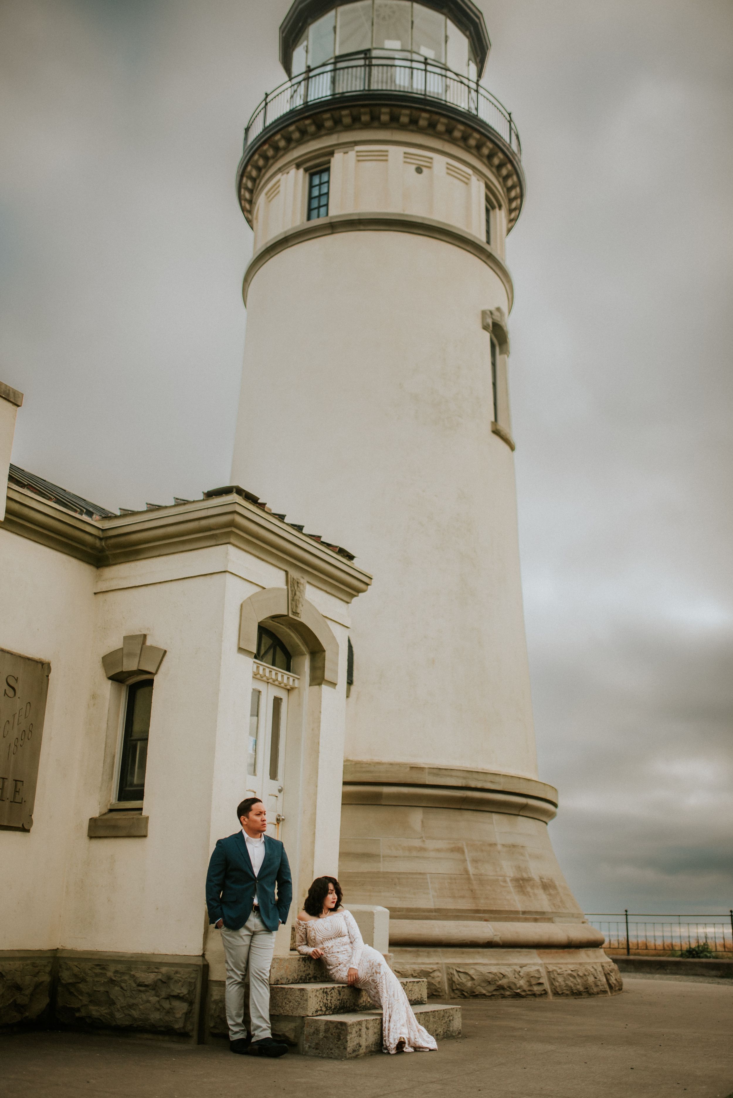 A couple in wedding attire posing in front of a lighthouse on a cloudy day on the coast of Washington State.