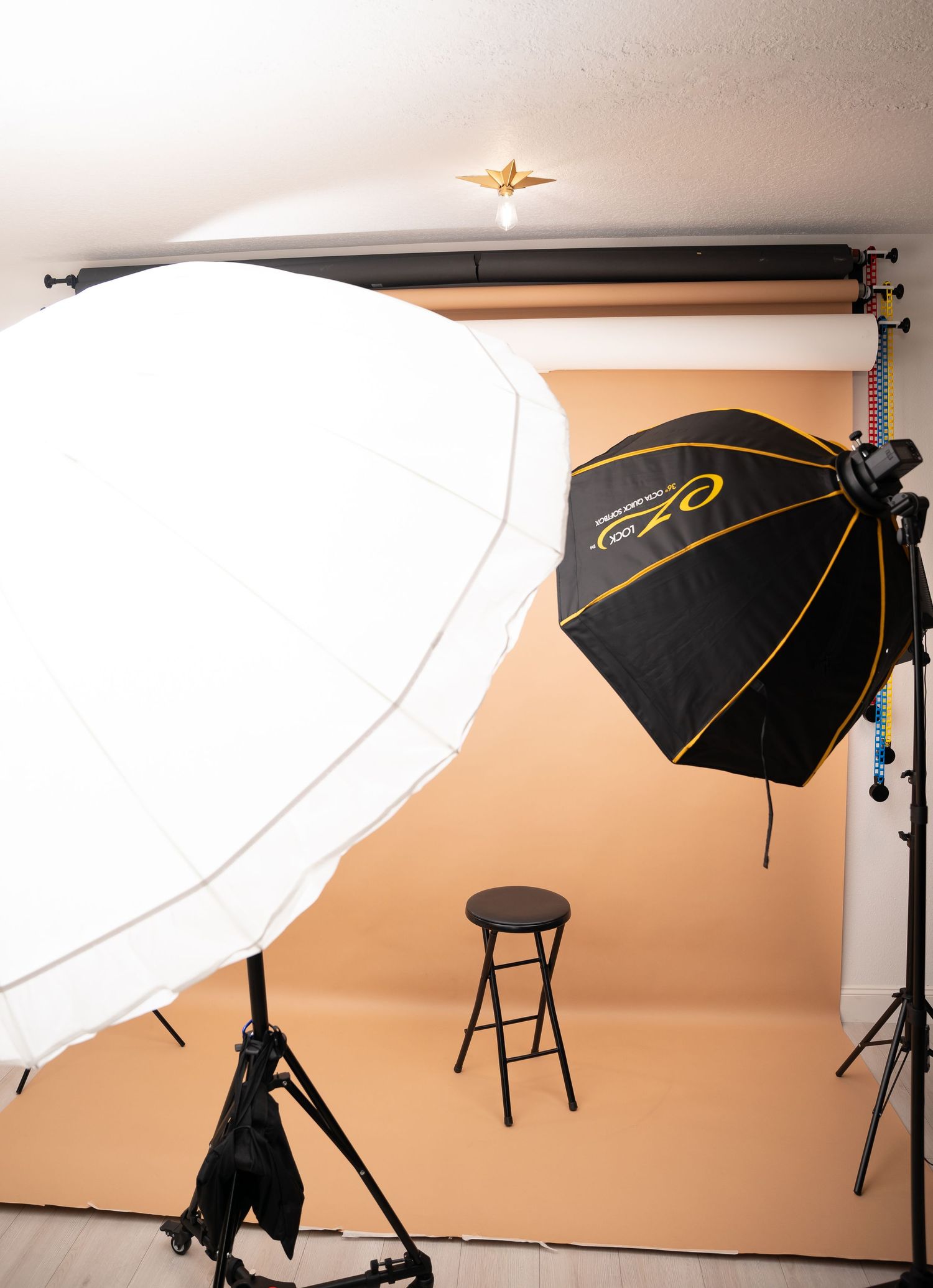 Professional photography studio setup with black umbrella lights and white reflectors against peach backdrop.