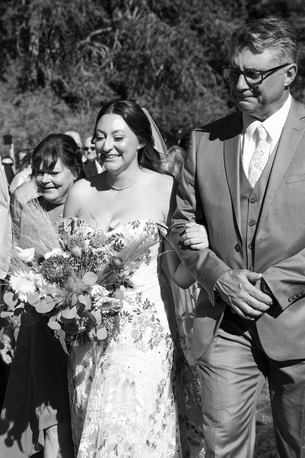 Wedding party members share a candid moment during an outdoor ceremony.