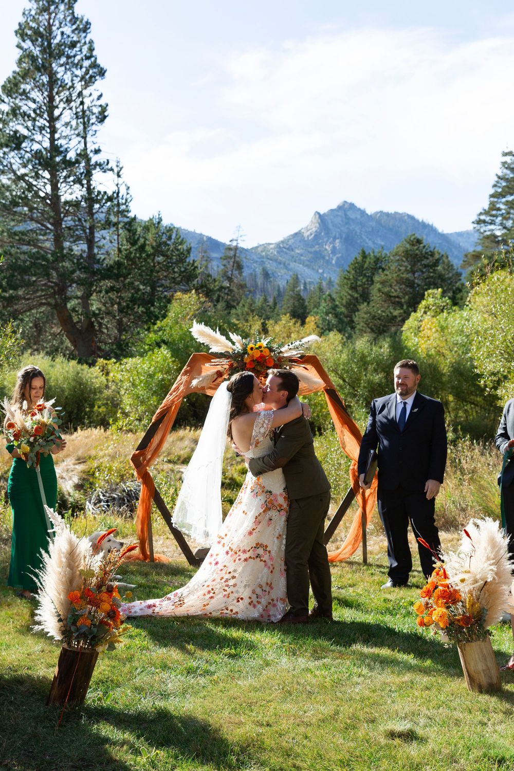 A wedding couple shares their first kiss under a rustic arch with mountain views.