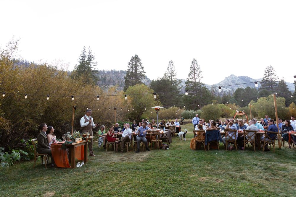 Wedding guests seated at tables during an outdoor reception in a mountainside setting.