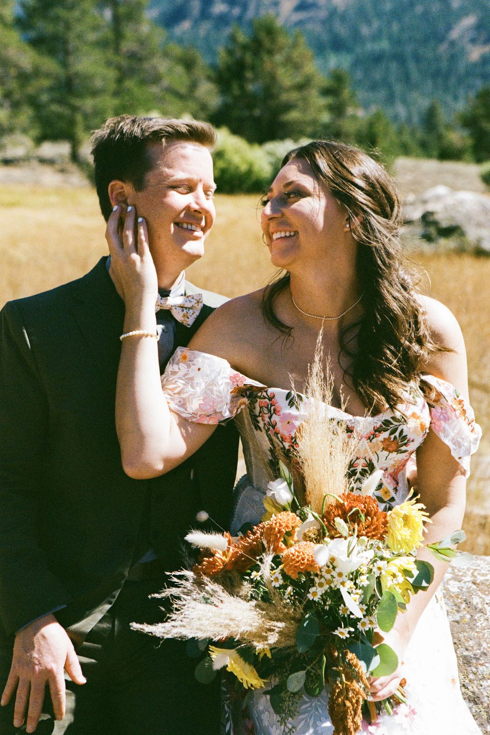 A joyful wedding couple shares an intimate moment in a scenic mountain meadow setting.