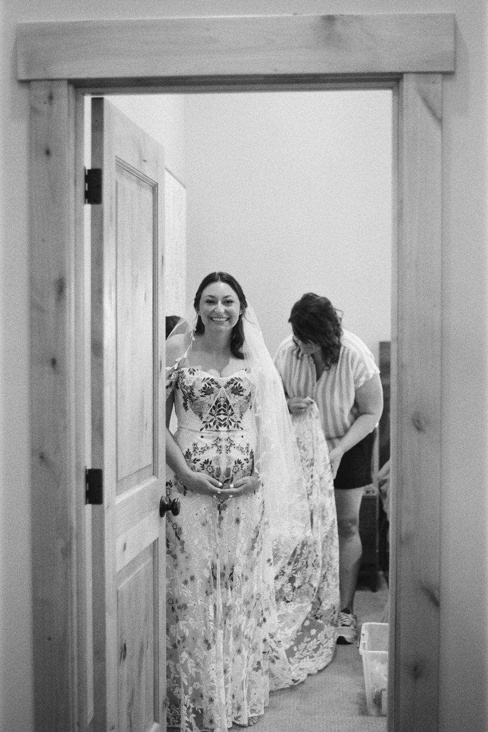 Black and white image of someone in a floral dress framed in a wooden doorway.