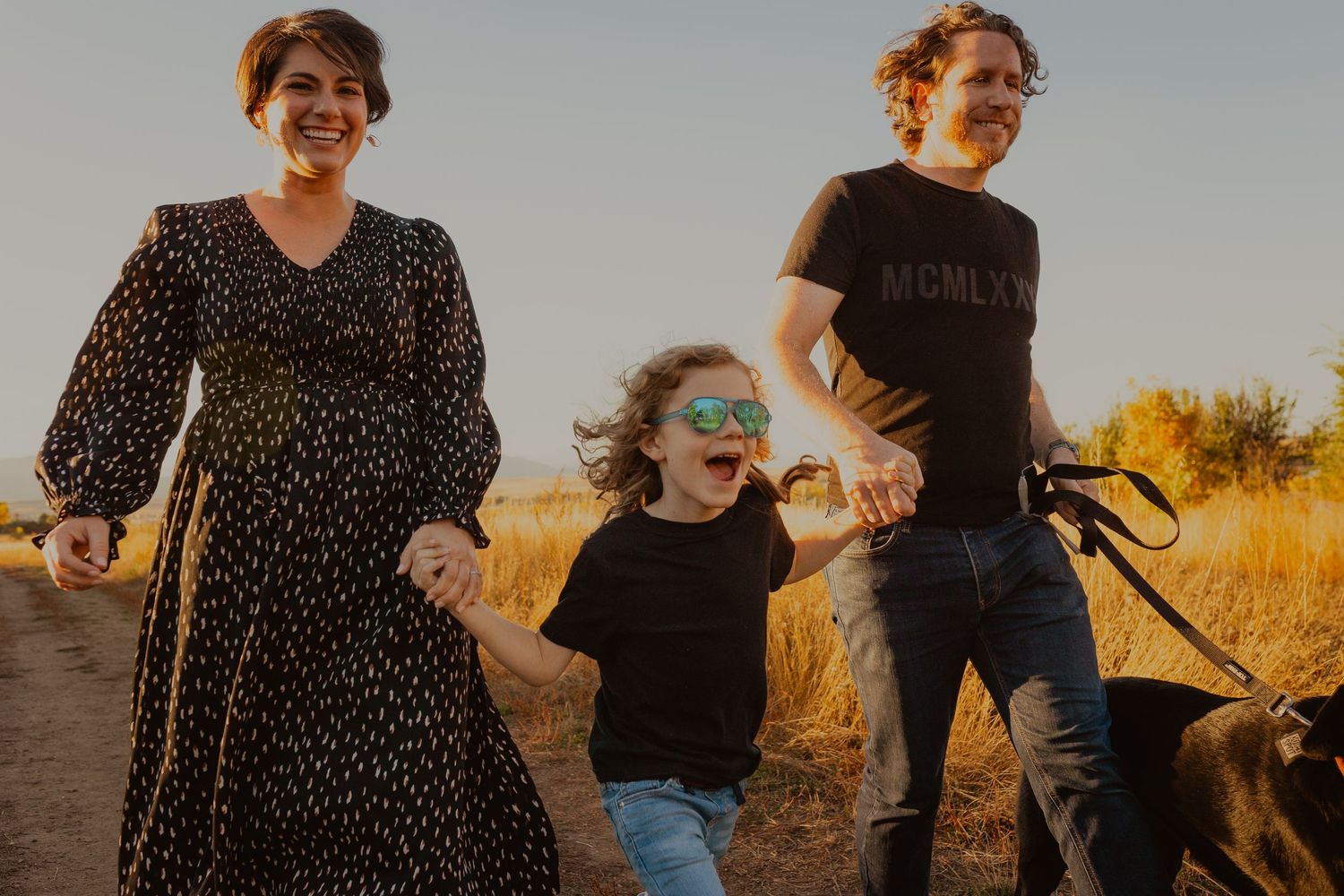A group of people laugh and walk together through a golden field at sunset.