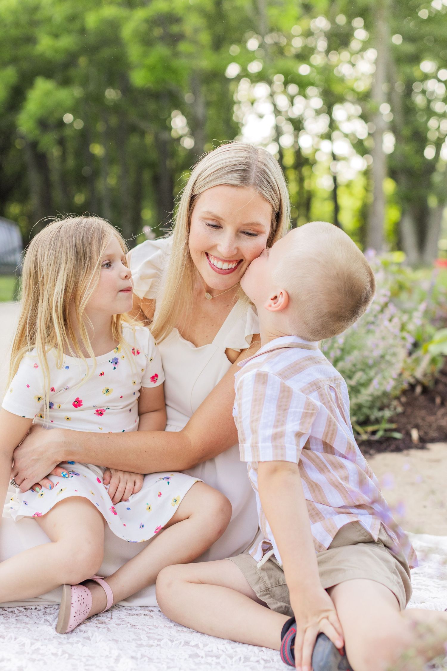 Family walking together on garden path surrounded by blooming spring flowers and evergreen trees in dreamy outdoor setting.
