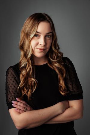 Professional studio portrait against dark background wearing black top with sheer polka dot sleeves.