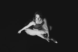 A ballet dancer performs a dramatic split leap in a tutu dress, captured in black and white against a dark background.