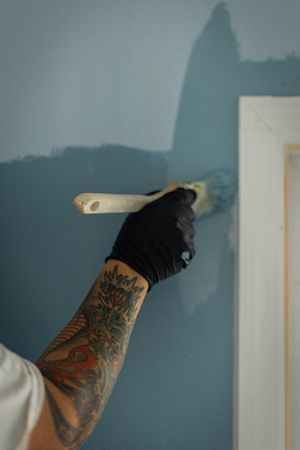 Sequence of photos showing a tattooed arm painting a wall in blue paint with a roller brush.
