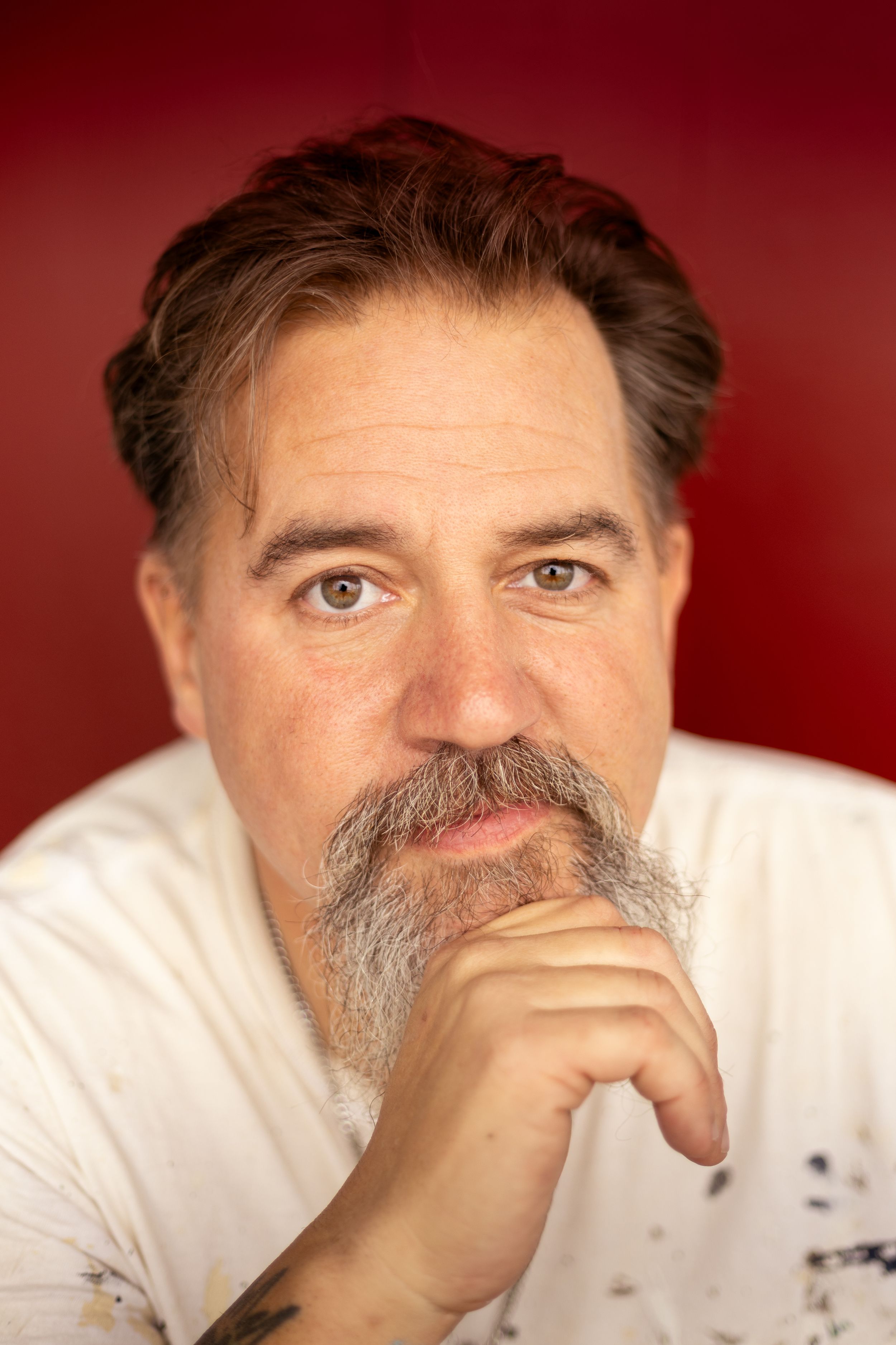 A series of close-up portraits showing someone with a gray beard wearing a white shirt against a dark red background.