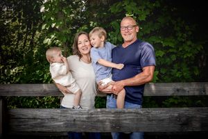 A family of four poses together against a wooden fence with lush greenery in the background.
