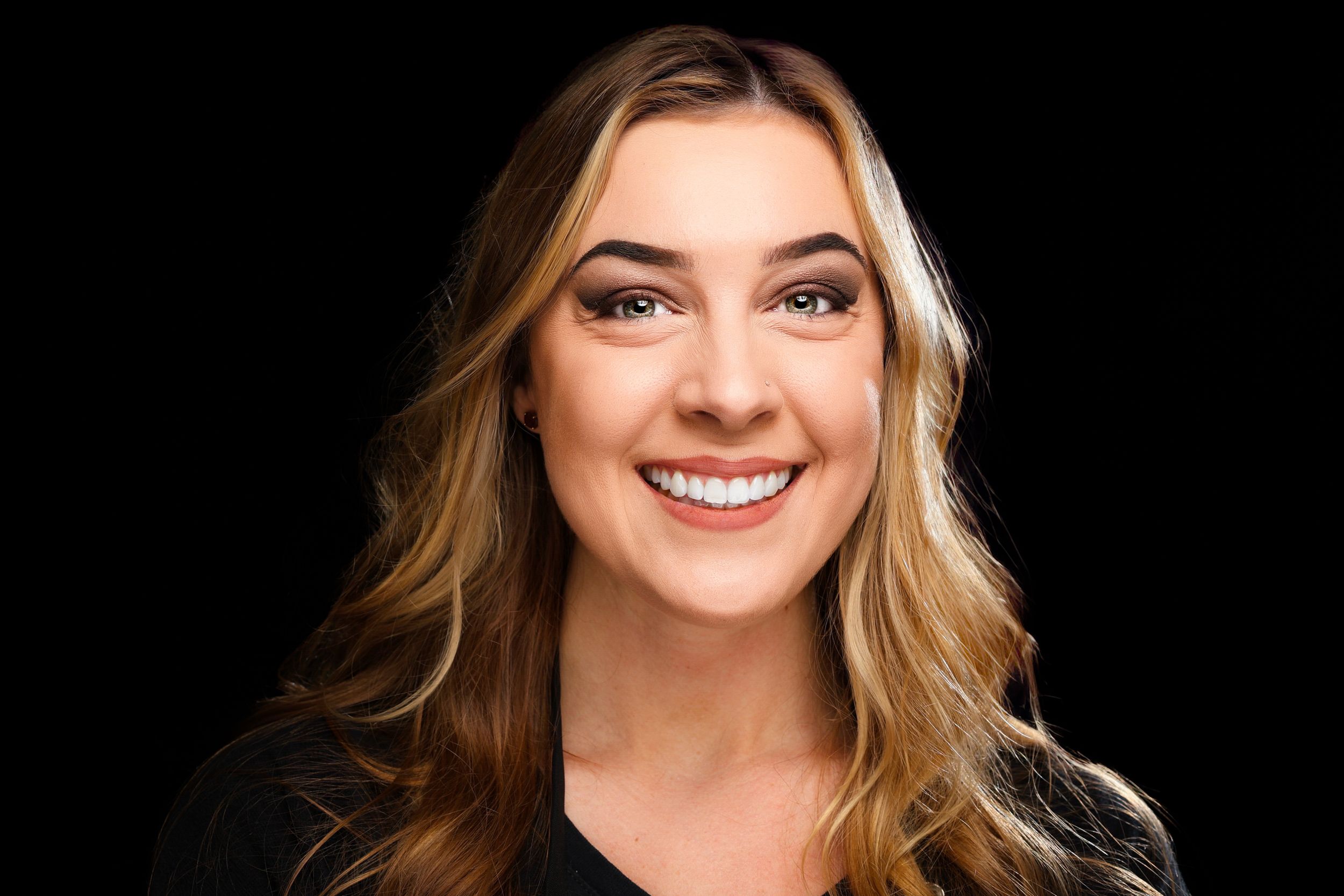 Portrait of a woman with blonde wavy hair and bright smile against black background.