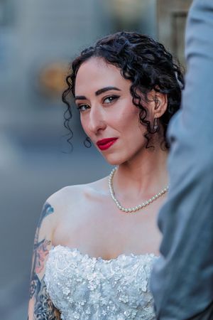 Close-up portrait of a bride wearing a white lace off-shoulder wedding dress and pearl necklace.
